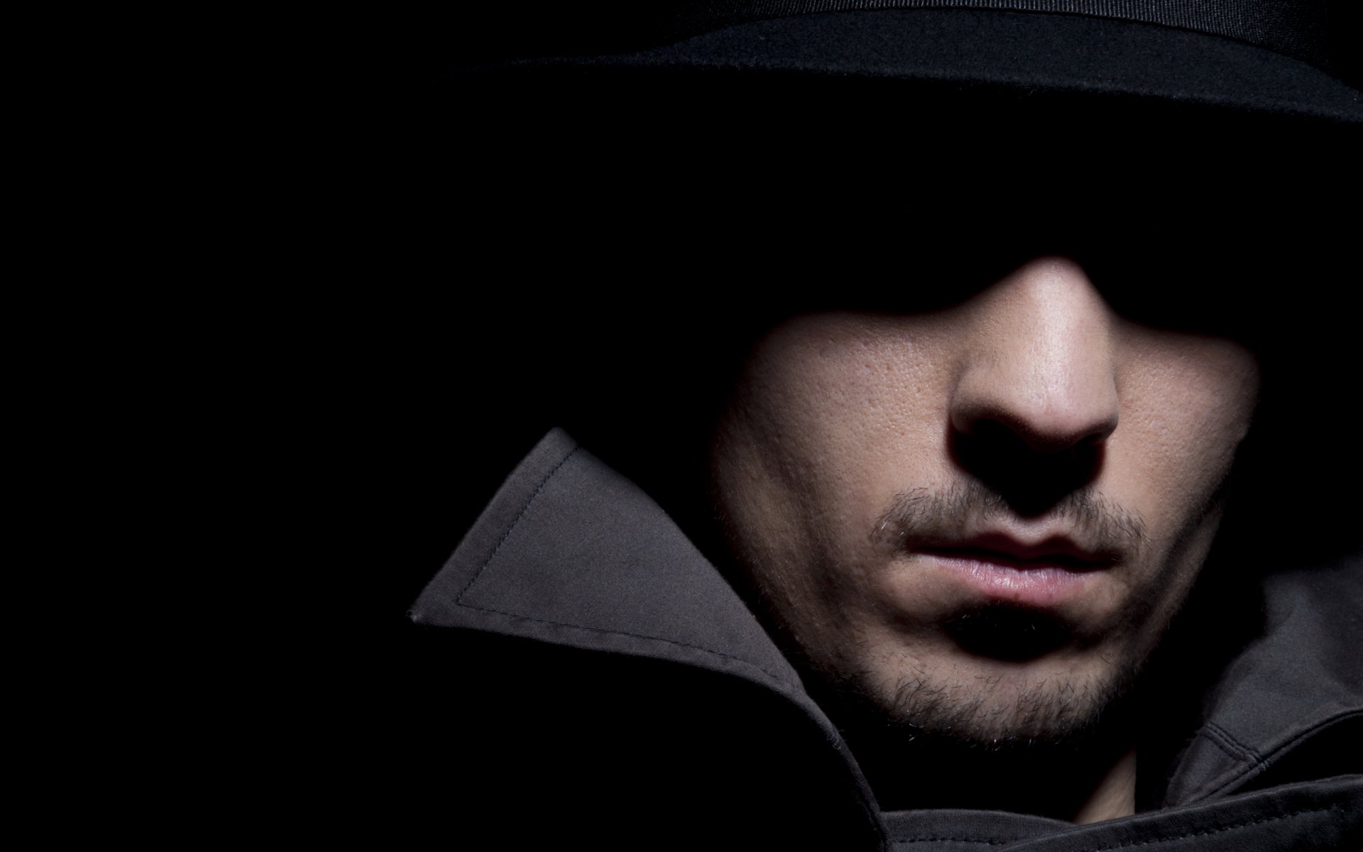 HD desktop wallpaper featuring a close-up of a man's face partially obscured by shadow and a hat, creating a mysterious and intense atmosphere.