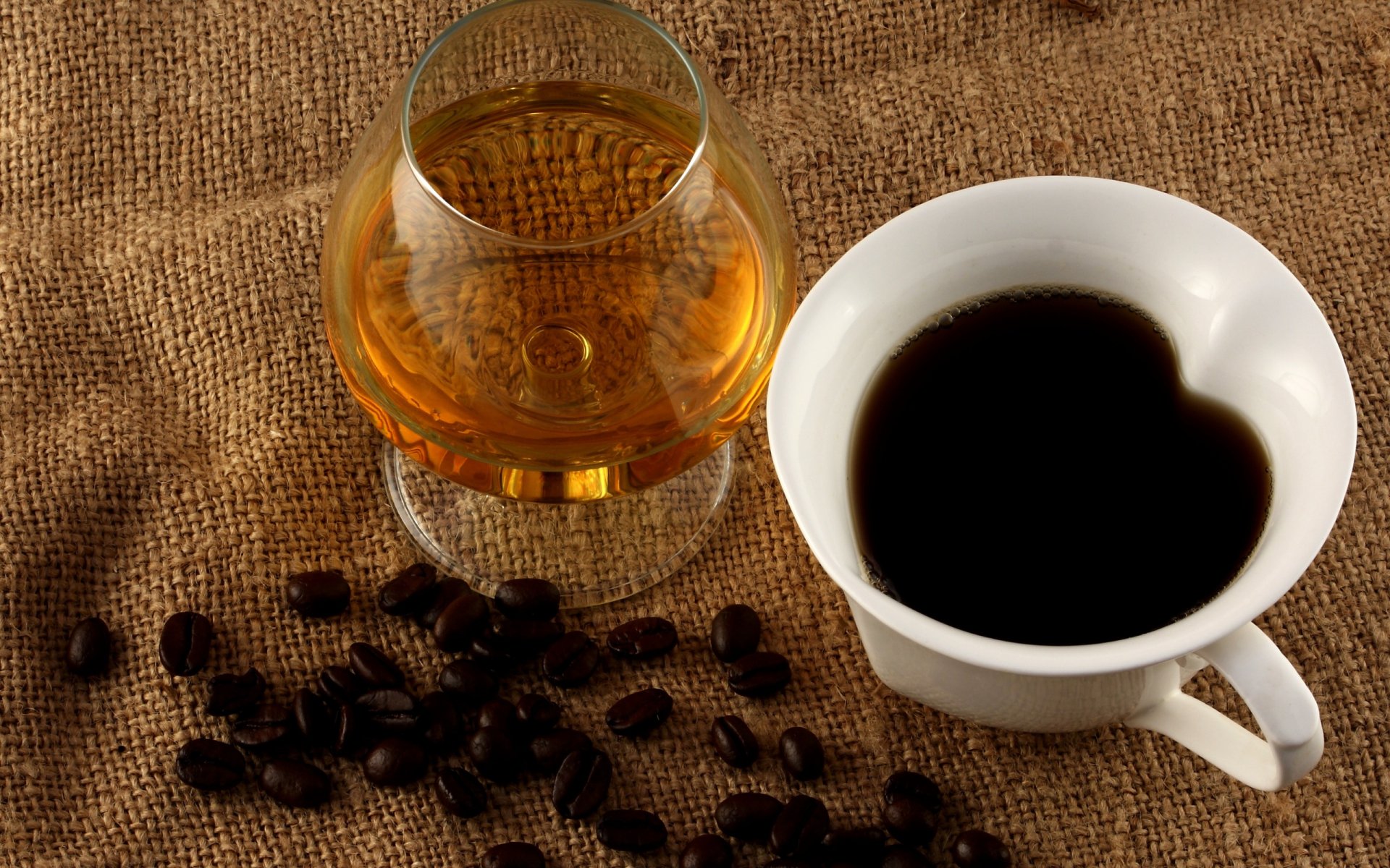 2K Quad HD PC desktop wallpaper featuring a food and coffee still life: white cup of black coffee, glass of amber liquid and scattered coffee beans on burlap background.