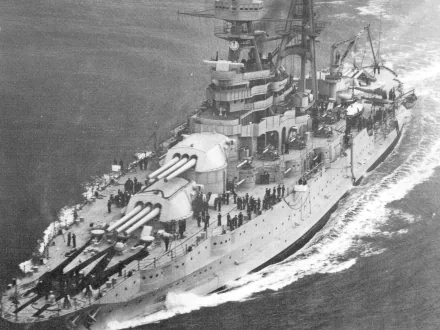 Black and white aerial view of the USS Arizona (BB-39) battleship at sea, showcasing its large guns and military crew onboard.