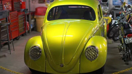 HD desktop wallpaper featuring a vibrant yellow Volkswagen Beetle parked in a garage with tools and motorcycles in the background.