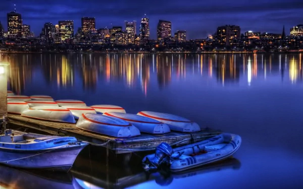 A serene view of Boston's skyline at night, reflecting on water, with boats docked in the foreground. This HD PC desktop wallpaper captures the city's vibrant man-made beauty.