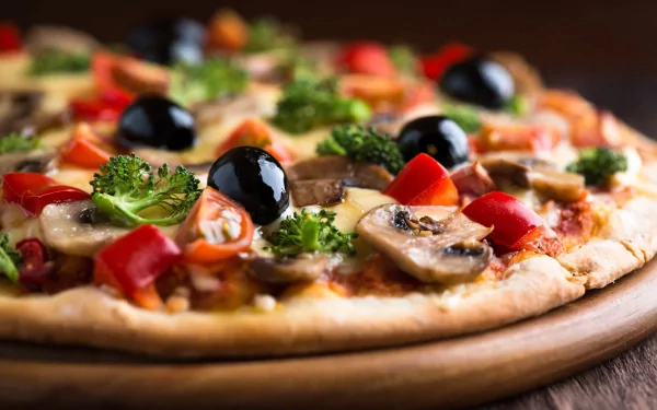 A delicious pizza topped with mushrooms, olives, tomatoes, and broccoli, presented on a wooden platter. This HD image serves as an attractive desktop wallpaper and background.