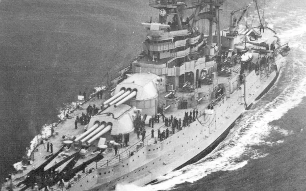 Black and white aerial view of the USS Arizona (BB-39) battleship at sea, showcasing its large guns and military crew onboard.