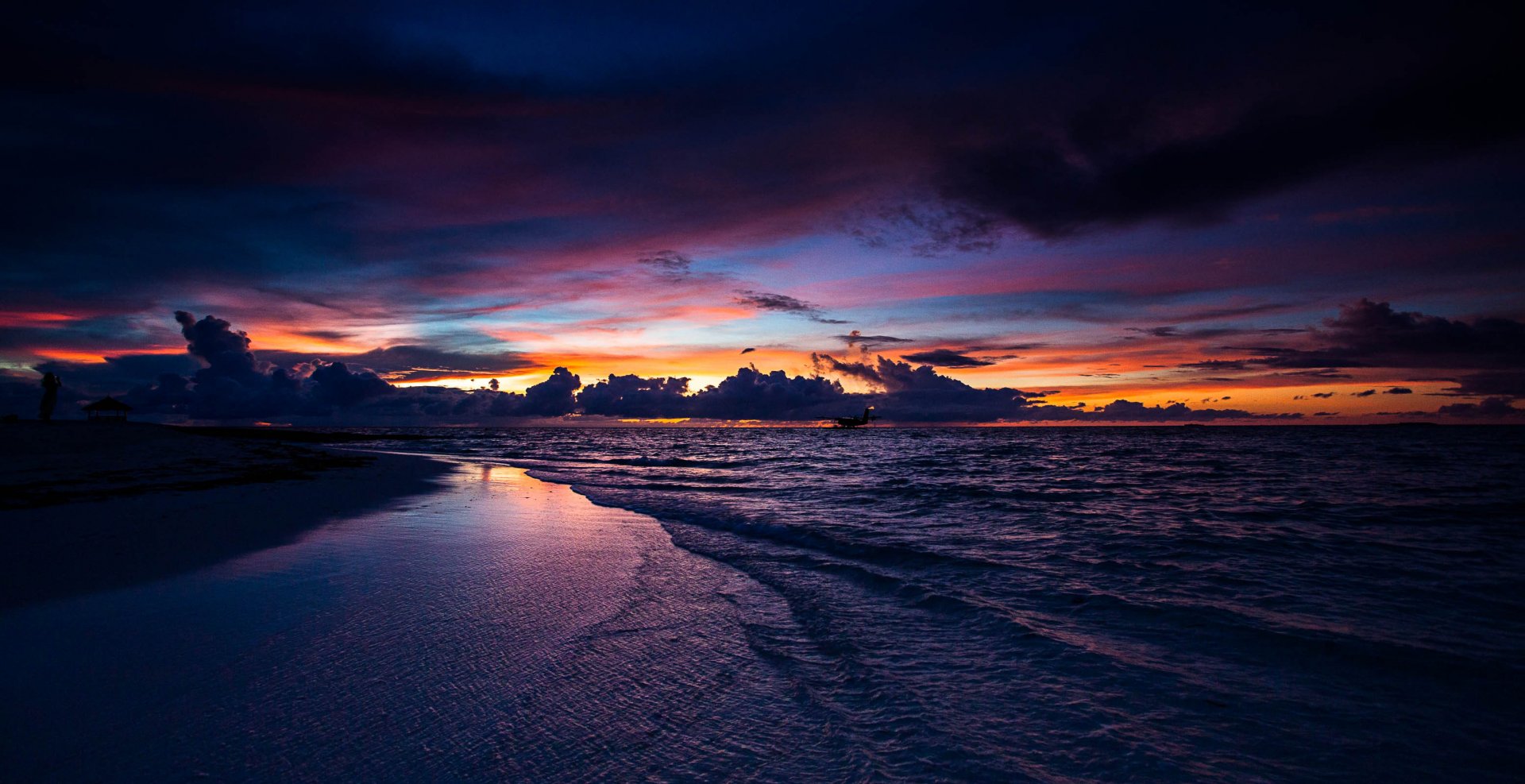 A serene beach at dusk, featuring a dramatic sky filled with vibrant colors reflecting on calm waters, creating a stunning nature-inspired HD desktop wallpaper.