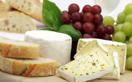 HD PC desktop wallpaper featuring a close-up of assorted cheeses, red and green grapes, fresh basil, and sliced bread arranged on a wooden board.