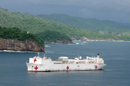 USNS Comfort (T-AH-20), white military hospital ship marked with red crosses, cruising past a green coastline — 4K Ultra HD PC desktop wallpaper/background.