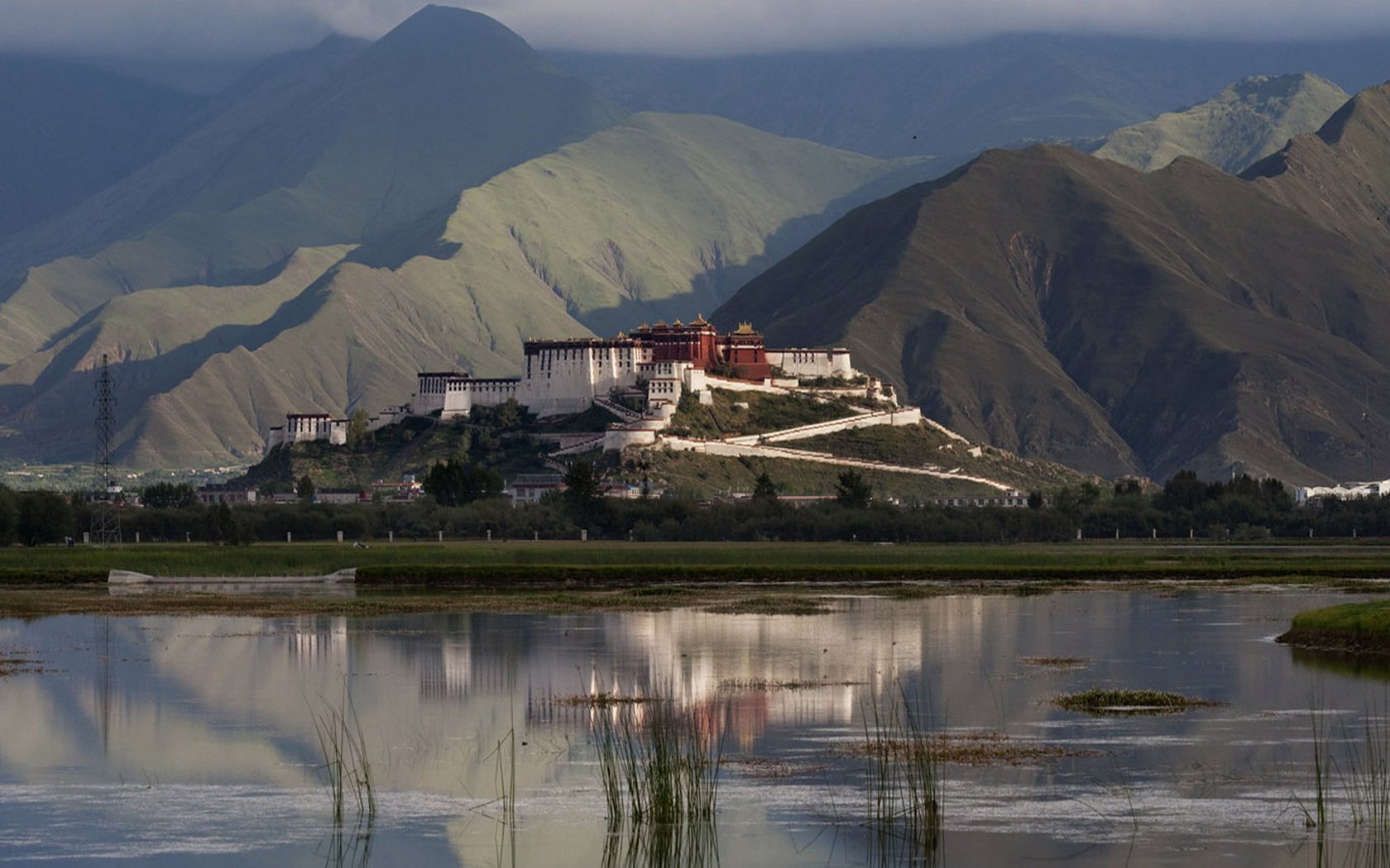 HD desktop wallpaper of a majestic man-made palace perched on a hillside, reflected in a calm body of water with sprawling mountains in the background.