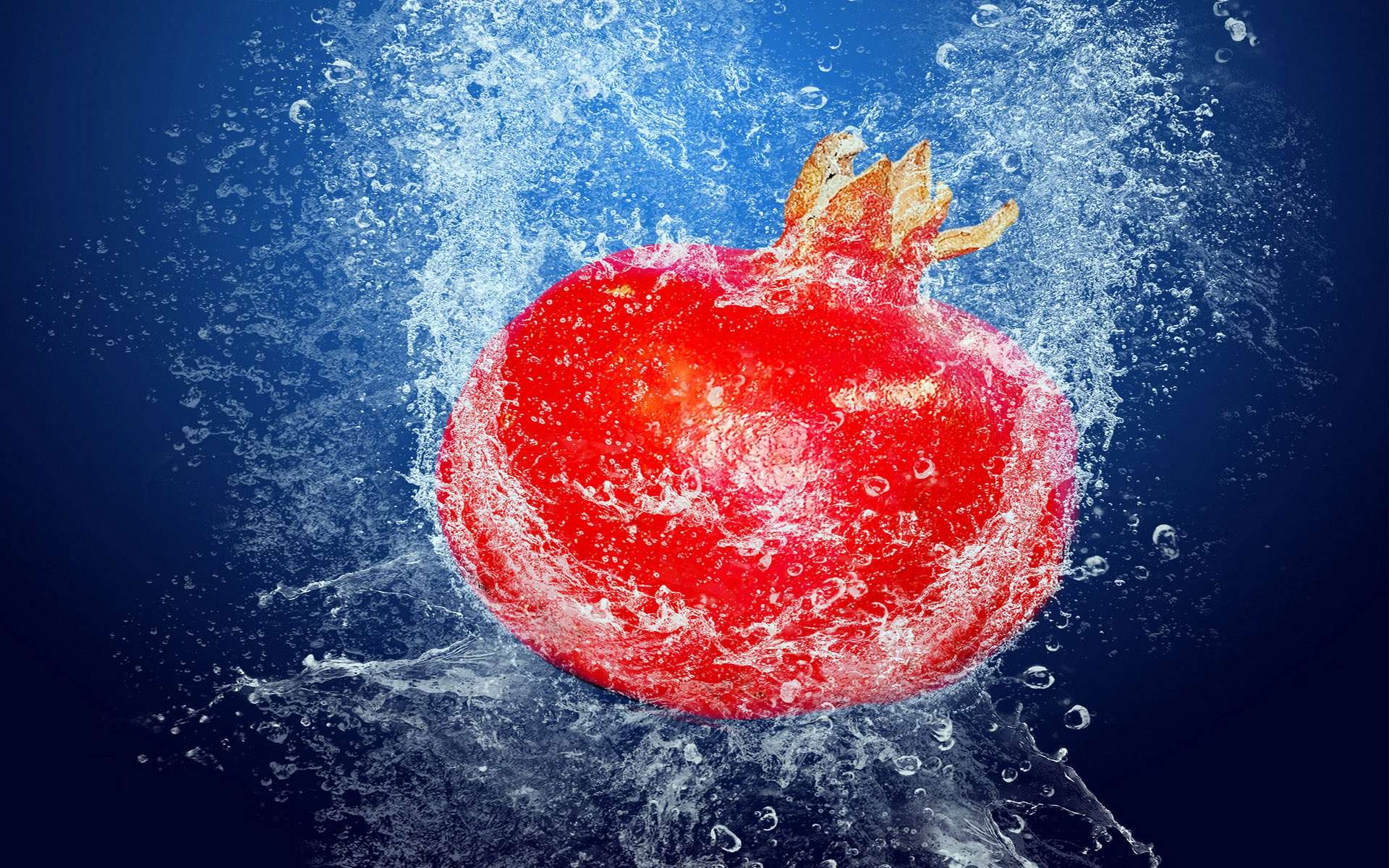 HD PC desktop wallpaper and background of a vibrant red pomegranate splashing in water against a deep blue backdrop, food-themed.