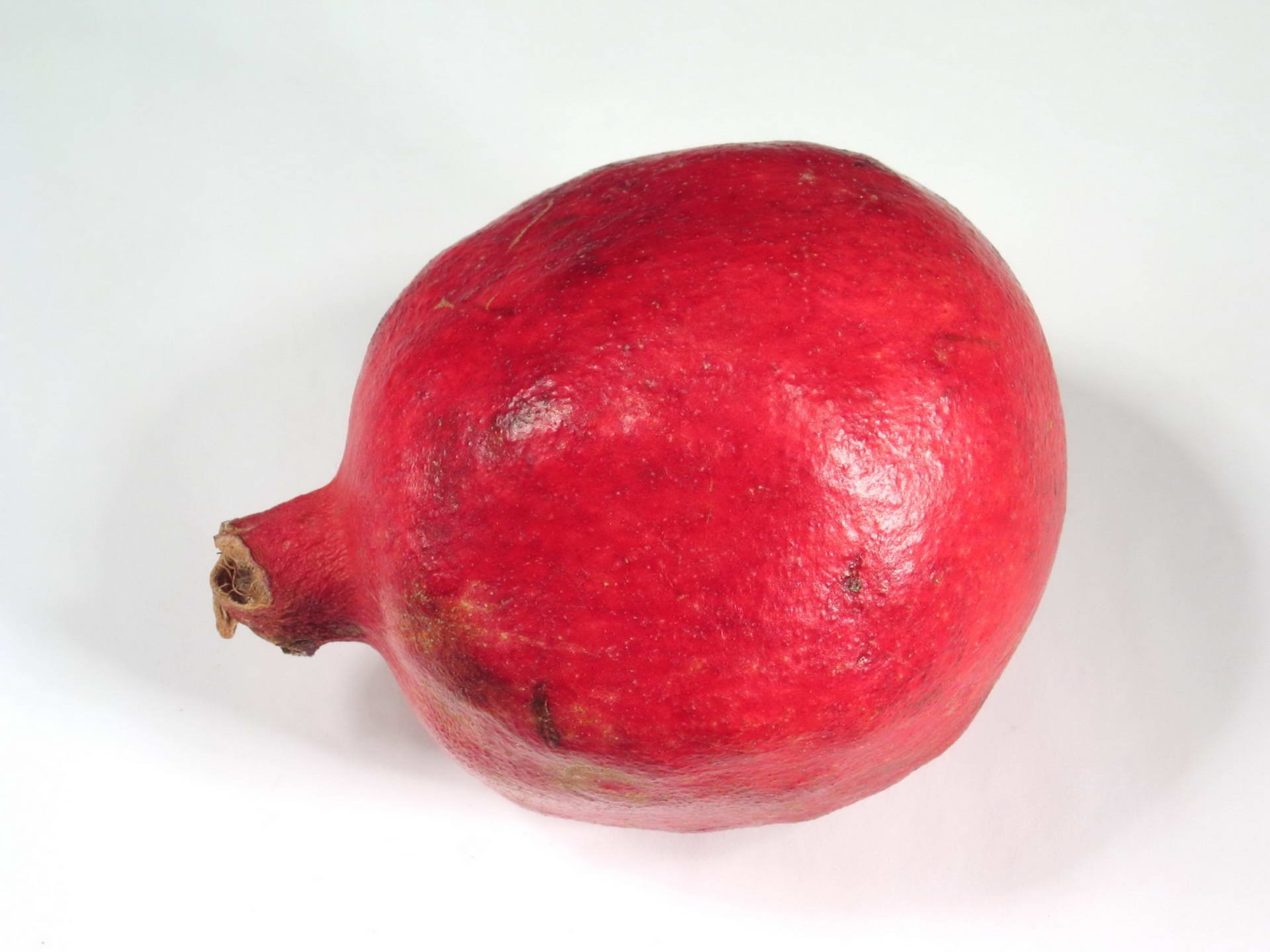 HD PC desktop wallpaper and background showing a single ripe red pomegranate on a clean white surface, food-themed.