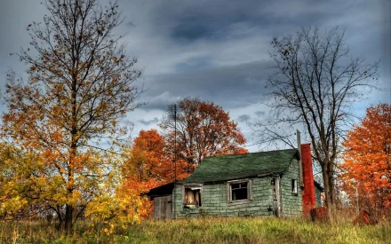 2K Quad HD PC desktop wallpaper and background: man-made green cabin with chimney in an autumn clearing, surrounded by colorful trees under a moody cloudy sky.