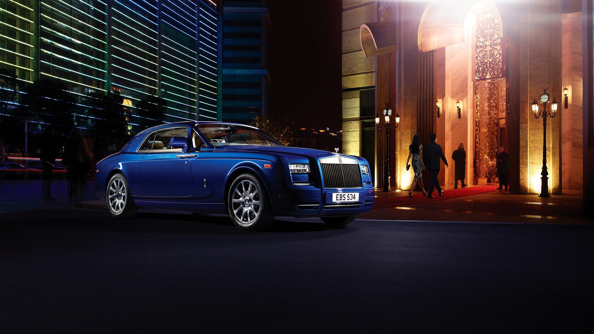HD PC desktop wallpaper of a blue Rolls-Royce Phantom Coupe vehicle parked at night outside an illuminated building, with pedestrian silhouettes.