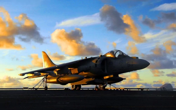 HD desktop wallpaper showing a McDonnell Douglas AV-8B Harrier II military jet on the runway during a vibrant sunset with scattered clouds.