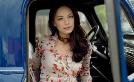 A captivating HD wallpaper featuring Kristin Kreuk, showcasing her natural beauty as she poses thoughtfully inside a vintage blue vehicle.