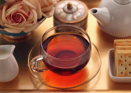 HD PC desktop wallpaper featuring a warm tea setting with a glass cup of tea, crackers, a white teapot, cream pitcher, and a bouquet of roses on a wooden surface.
