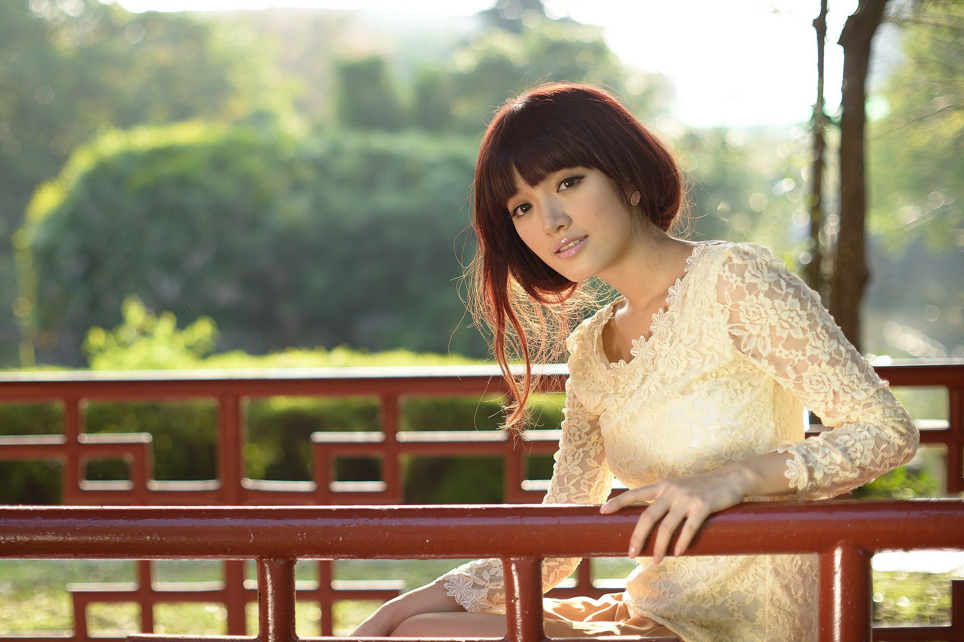 HD desktop wallpaper featuring an Asian woman in a lacy white dress, leaning on a red railing with lush greenery in the background.
