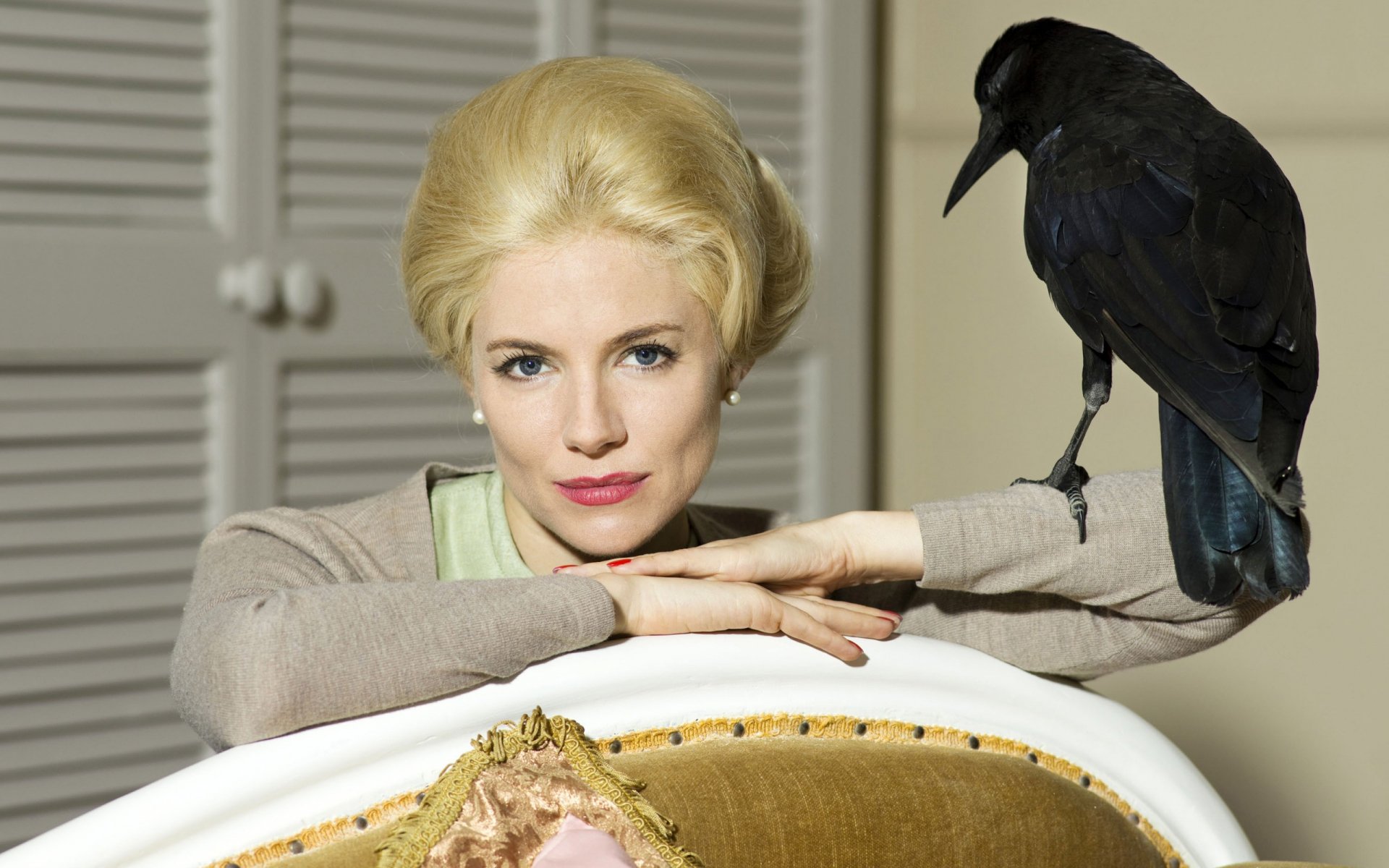 Blonde woman posed with a black crow perched on an ornate chair, elegant studio portrait — 2K Quad HD PC desktop wallpaper and background.