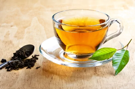 A clear glass cup of amber tea on a saucer beside loose tea leaves and a green tea leaf, captured in 4K Ultra HD as a PC desktop wallpaper and background.