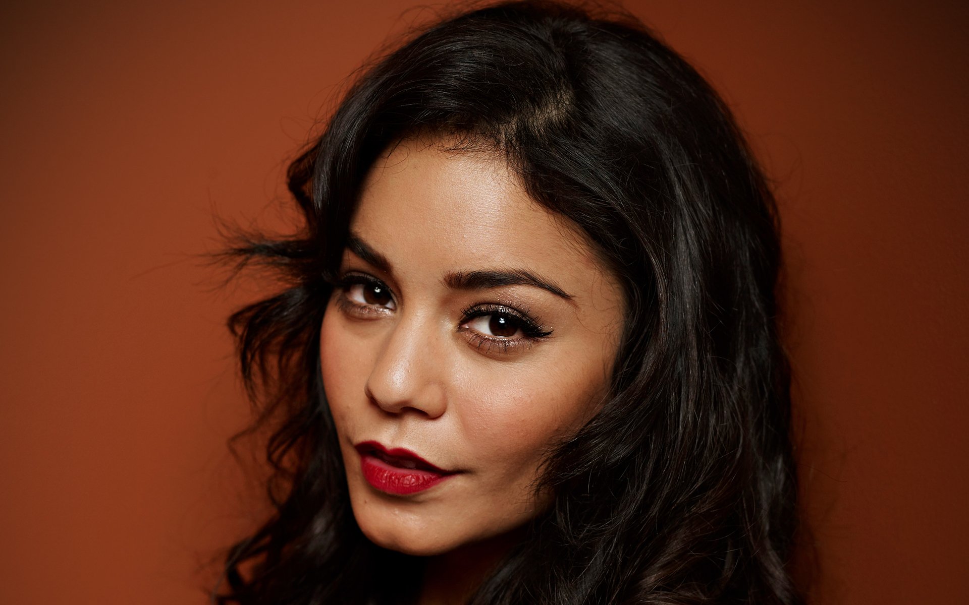 HD PC desktop wallpaper featuring celebrity Vanessa Hudgens with dark hair and bold red lipstick against a warm brown background.