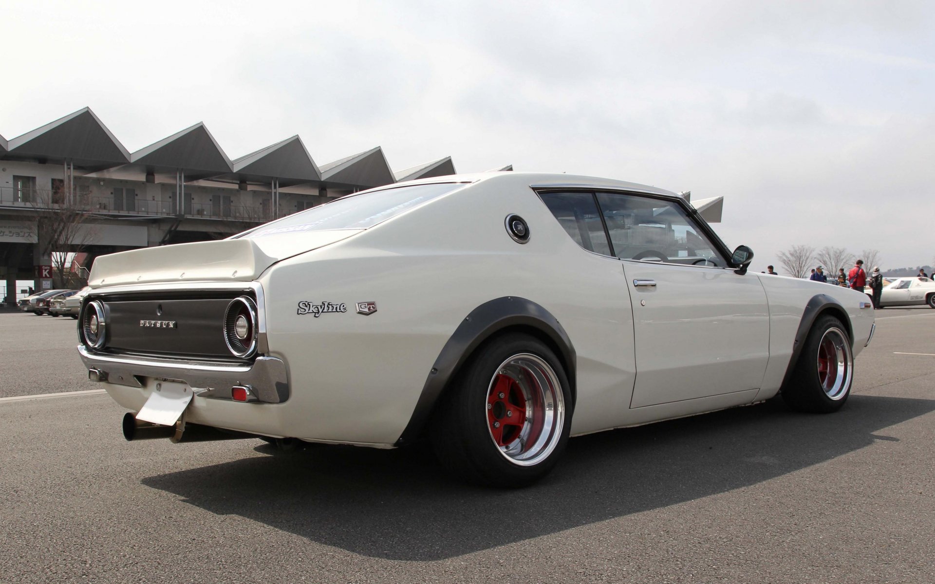 HD desktop wallpaper featuring a white Nissan Skyline parked outdoors, showcasing its classic design and sleek curves against a cloudy sky background.