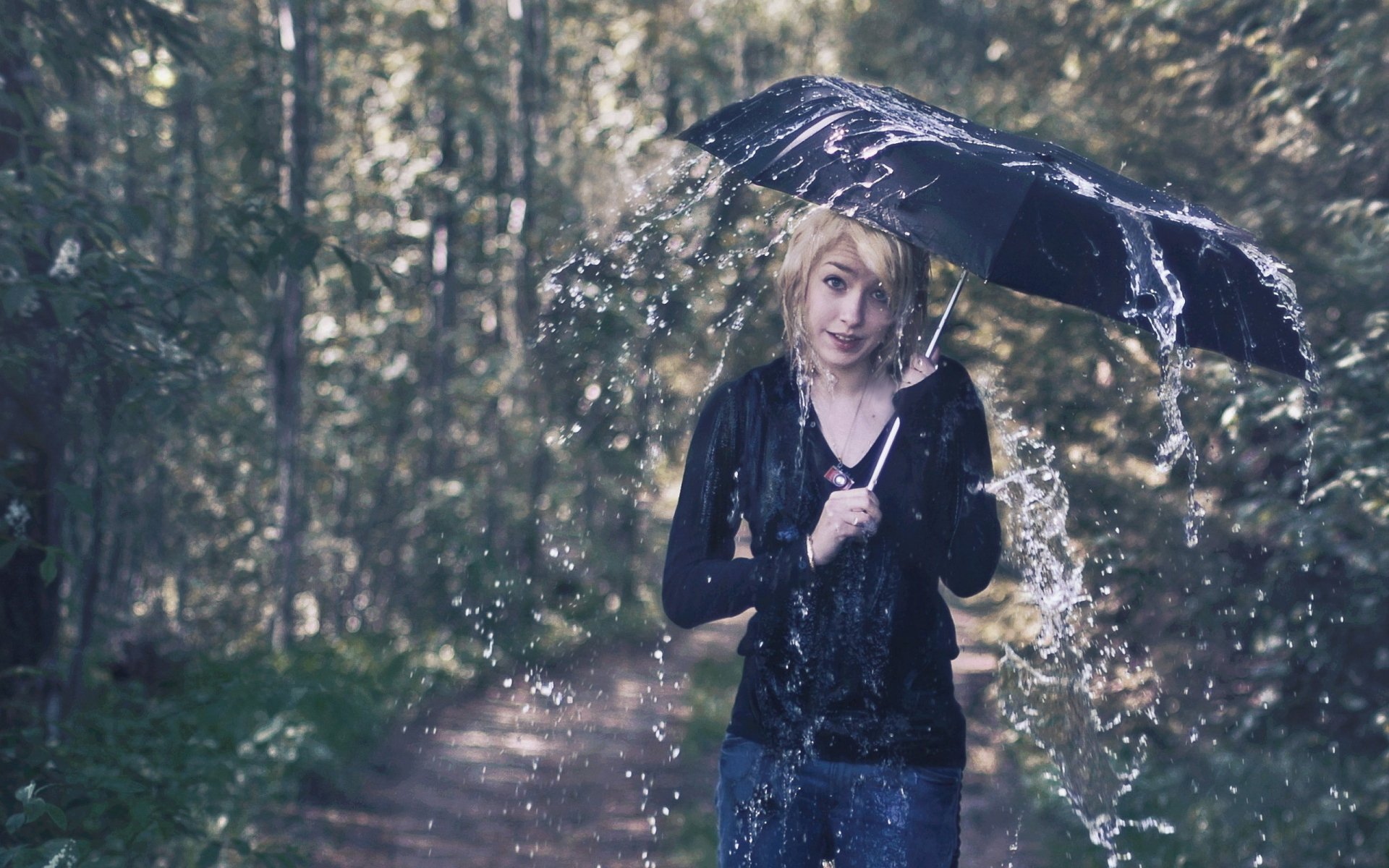 A person holding a black umbrella in the rain on a forest path, captured in a high-definition photography image used as a PC desktop wallpaper.
