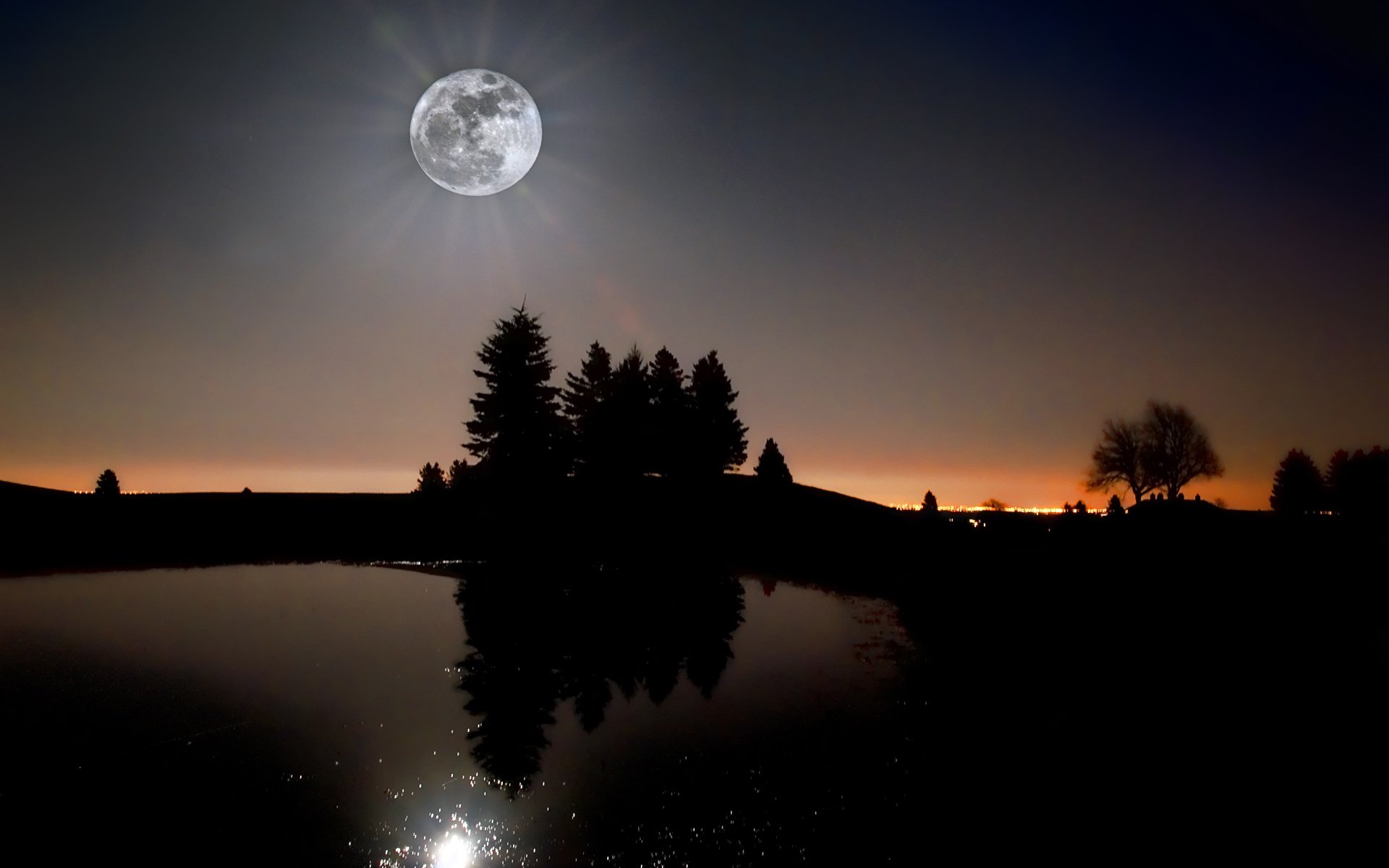 HD nature desktop wallpaper featuring a full moon rising over silhouetted trees, reflected peacefully in a calm body of water at dusk.