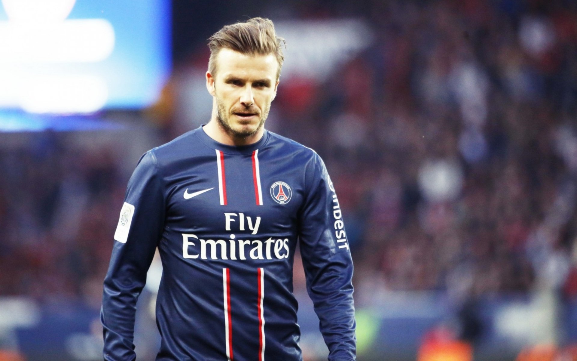 David Beckham in a Paris Saint-Germain jersey during a match, captured in a high-definition wallpaper. A dynamic sports-themed background showcasing his iconic presence.