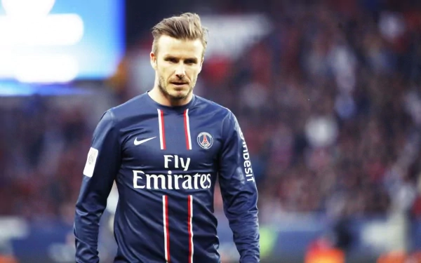 David Beckham in a Paris Saint-Germain jersey during a match, captured in a high-definition wallpaper. A dynamic sports-themed background showcasing his iconic presence.