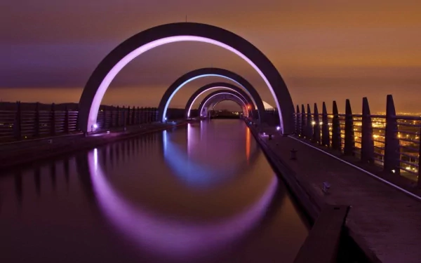 A stunning view of the Falkirk Wheel in Scotland, featuring its illuminated arches reflected in the still water, showcasing an impressive feat of man-made engineering at night.