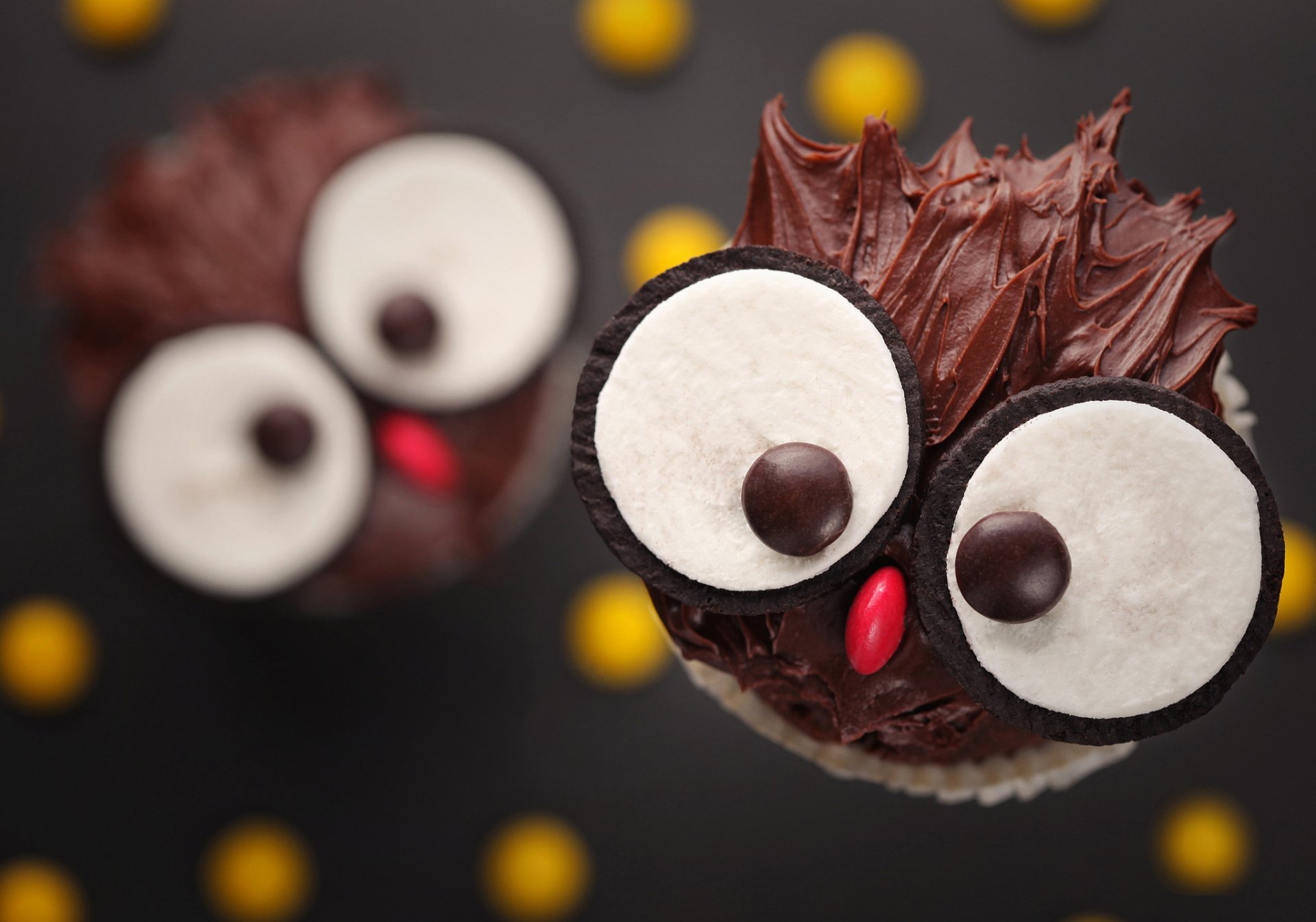Whimsical chocolate cupcakes designed to look like cute owls, featuring large eyes and vibrant decorations, against a dark backdrop with colorful dots. HD desktop wallpaper.