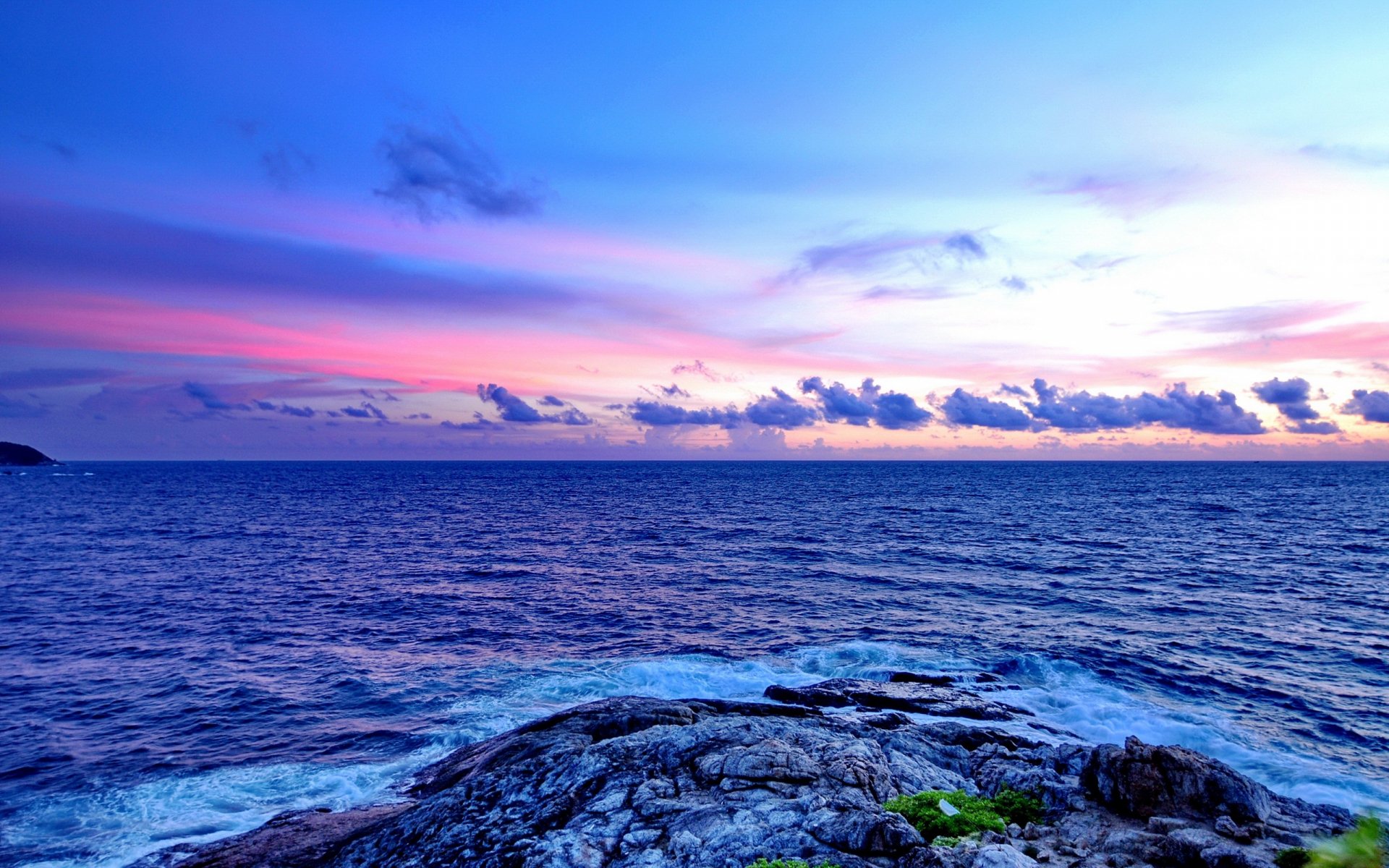 HD desktop wallpaper showcasing a serene ocean shore at dusk, with a colorful sunset sky blending clouds and horizon over the calm sea.