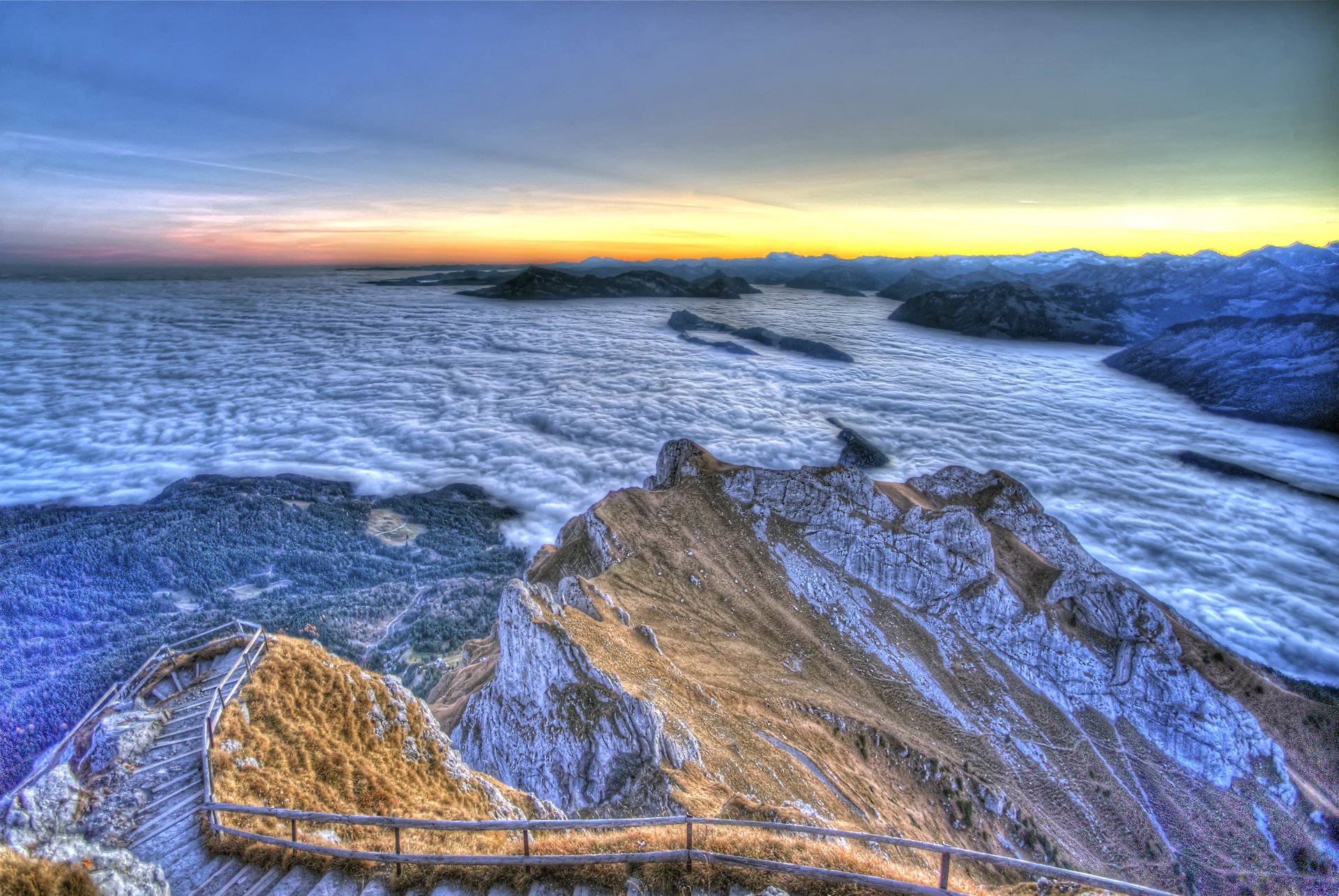 HD desktop wallpaper showing a man-made stair path winding along a rugged coastal cliff at sunset with ocean waves in the background.