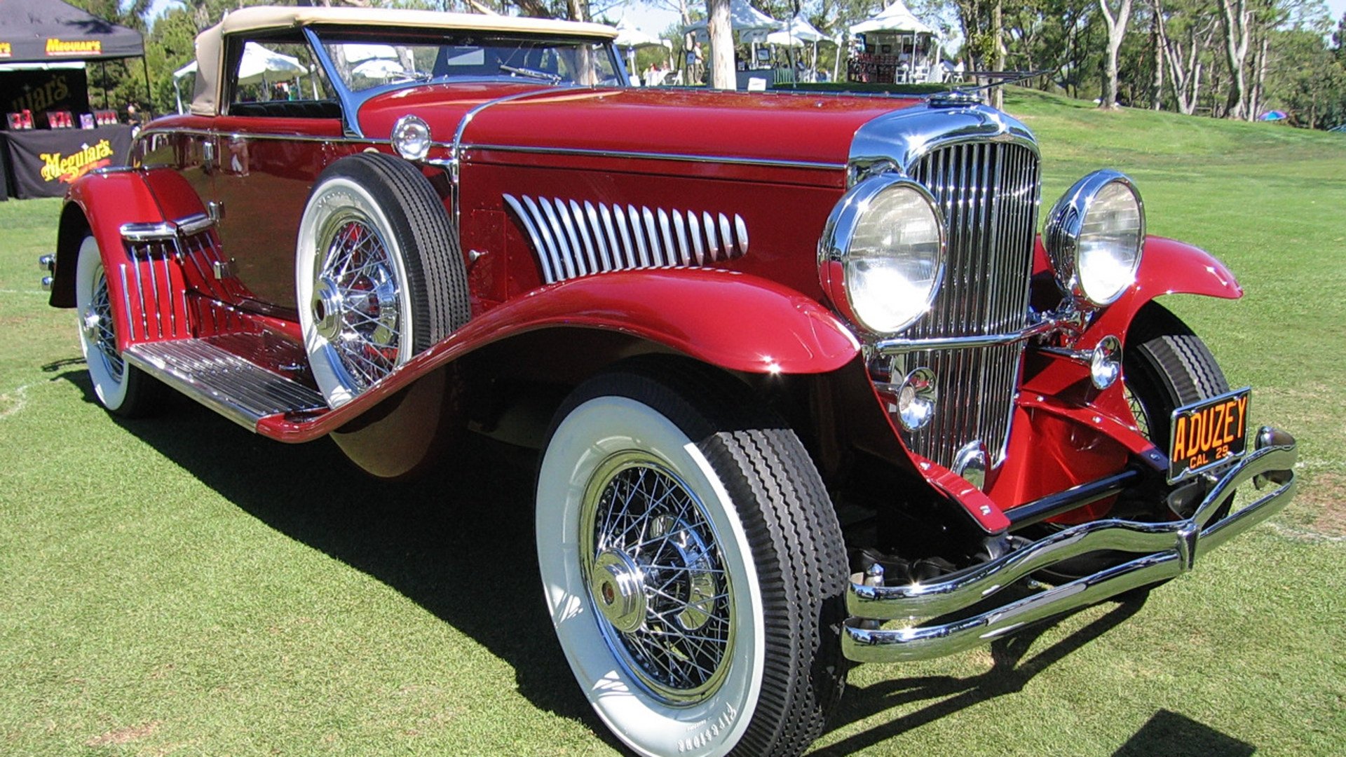 A classic red Duesenberg vintage vehicle displayed outdoors, featured as an HD PC desktop wallpaper and background with detailed chrome and whitewall tires.
