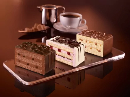 A tempting display of chocolate desserts, featuring layered cakes in rich flavors, set against a warm background with a cup of coffee, creating an inviting atmosphere for food lovers.