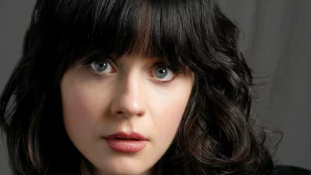 Close-up portrait of Zooey Deschanel, featuring her signature bangs and expressive eyes, set against a soft background. This high-definition image serves as a striking desktop wallpaper.
