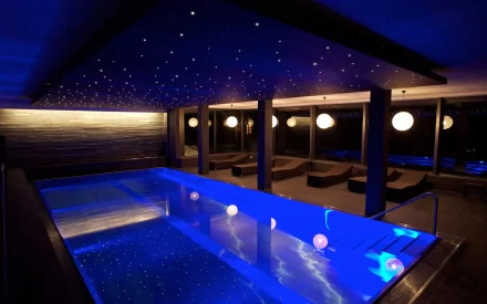 HD desktop wallpaper of a man-made indoor pool illuminated by blue lights and small ceiling stars, surrounded by dark wooden walls and round hanging lamps.