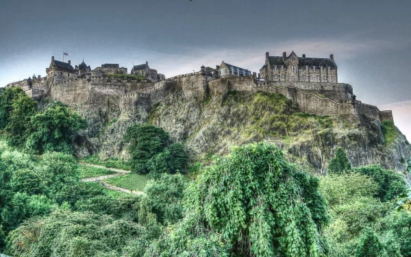 HD PC desktop wallpaper showcasing a majestic man-made castle perched atop a rocky hill, surrounded by lush green trees under a cloudy sky.
