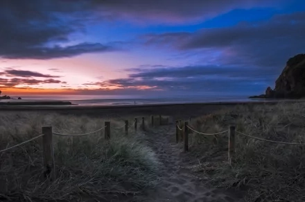 A tranquil path leading to a beach at sunset, surrounded by gentle dunes and a dramatic sky, creating a serene nature scene for a stunning HD desktop wallpaper.