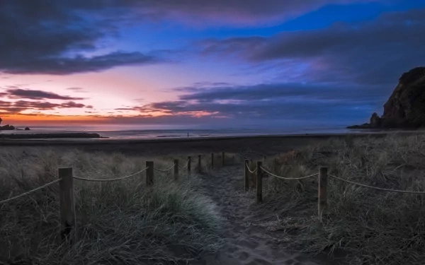 A tranquil path leading to a beach at sunset, surrounded by gentle dunes and a dramatic sky, creating a serene nature scene for a stunning HD desktop wallpaper.
