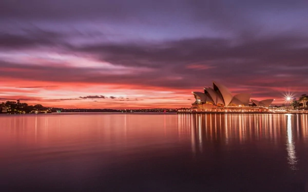 A stunning view of the Sydney Opera House at sunset, reflecting on the calm waters, capturing the beauty of Sydney's iconic man-made architecture.