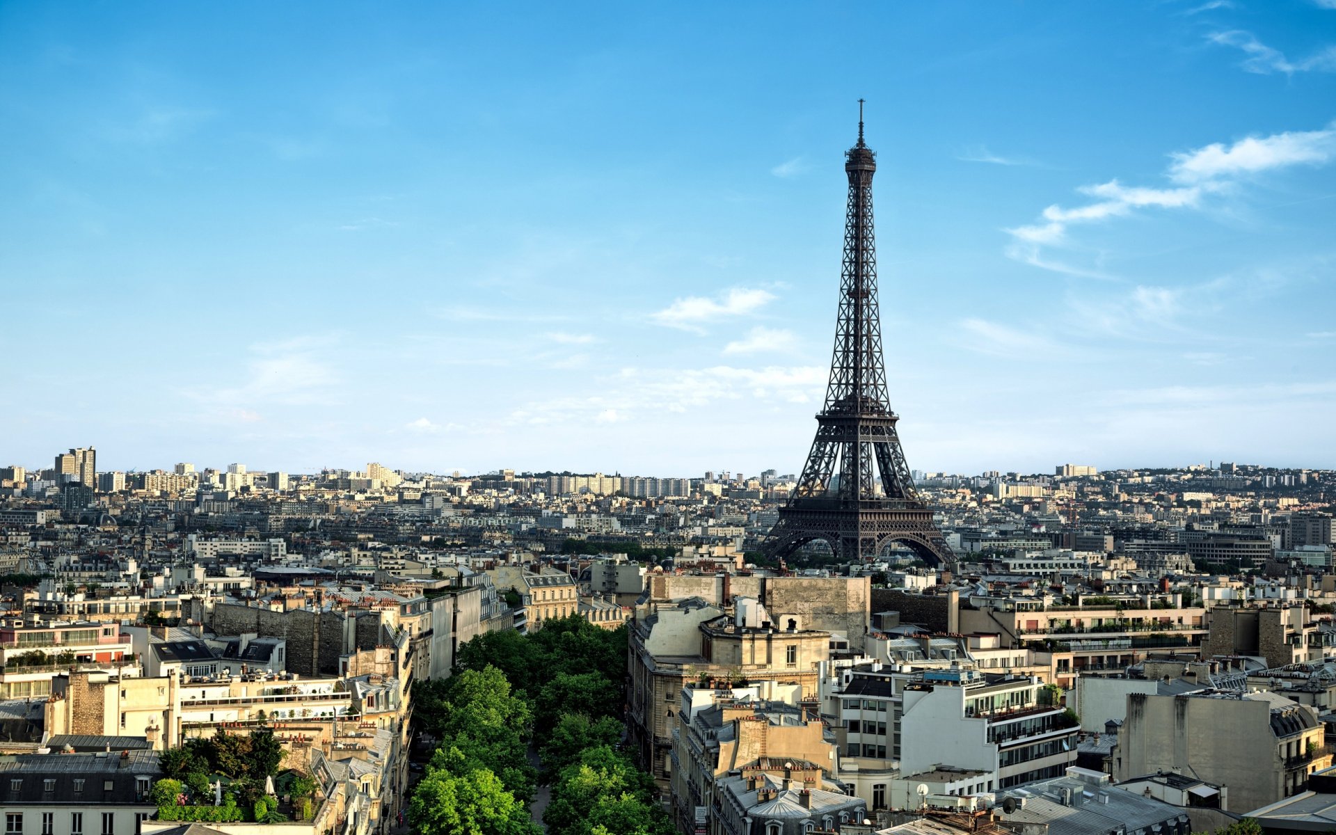 A panoramic view of the Eiffel Tower against a clear blue sky, surrounded by Parisian architecture and greenery, showcasing the beauty of France's iconic landmark.