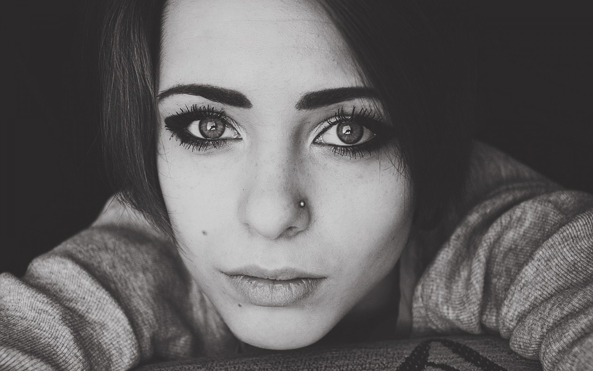 Black-and-white close-up of a young woman's face—intense eyes and nose stud—2K Quad HD PC desktop wallpaper/background.
