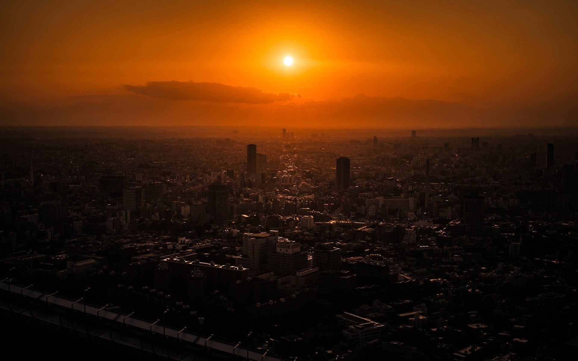 HD desktop wallpaper capturing a stunning sunset over the man-made skyline of Tokyo, with warm orange hues illuminating the cityscape.