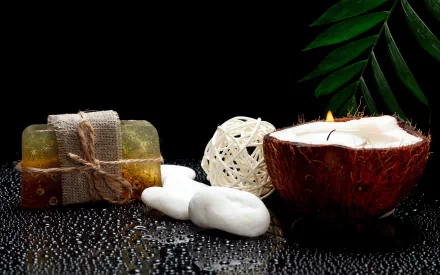 HD desktop wallpaper featuring a man-made spa setting with soap bars, a lit candle in a coconut shell, decorative spheres, and green leaves on a reflective black surface.