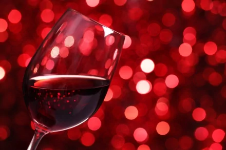A close-up of a wine glass filled with red wine, set against a vibrant backdrop of shimmering red bokeh, creating an elegant and inviting atmosphere for food and wine lovers.