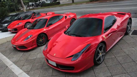 HD PC desktop wallpaper featuring a lineup of vibrant red Ferrari sports cars parked on a city street.