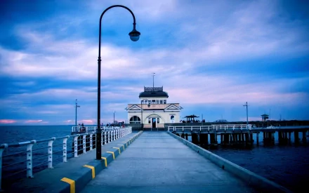 An HD desktop wallpaper featuring a serene pier scene with a classic lamp post, illuminated against a dramatic blue sky, blending nature and man-made architecture.