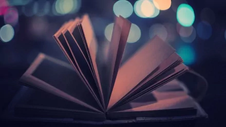 An HD desktop wallpaper featuring an open book with pages fanned out against a blurred background of colorful lights.