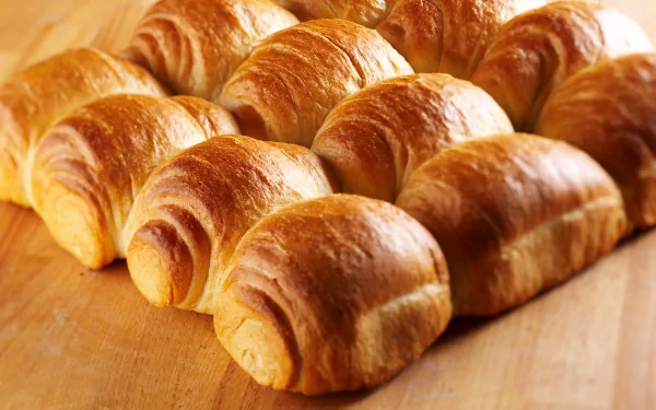 A warm assortment of freshly baked bread rolls, showcasing a golden-brown crust, arranged neatly on a wooden surface. This 4K Ultra HD image captures the essence of baking and delicious food.