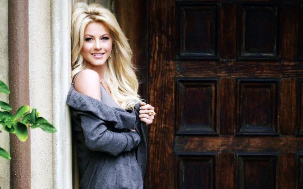 Julianne Hough smiles playfully while leaning against a rustic door, her long blonde hair cascading around her shoulders, creating an engaging HD desktop wallpaper background.
