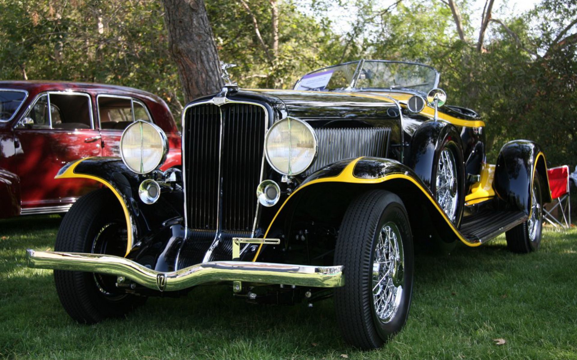 2K Quad HD PC desktop wallpaper of a glossy black-and-yellow vintage car, a classic vehicle parked on grass at an outdoor car show.